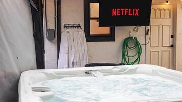 Una vasca idromassaggio con acqua corrente, un cartello con scritto 'NETFLIX' e un portascopevoli con asciugamani.
