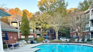 A swimming pool with lounge chairs, a brick patio, and surrounding buildings. - Chic Blue Apt w Patio + Pool, Free Parking, 10 min to ATL (Atlanta)