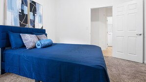 A bedroom with a blue bed, white walls, and a door leading to another room. - Chic Blue Apt w Patio + Pool, Free Parking, 10 min to ATL (Atlanta)