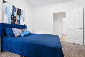 Ein Schlafzimmer mit einem blauen Bett, weißen Wänden und einer Tür zu einem anderen Raum.