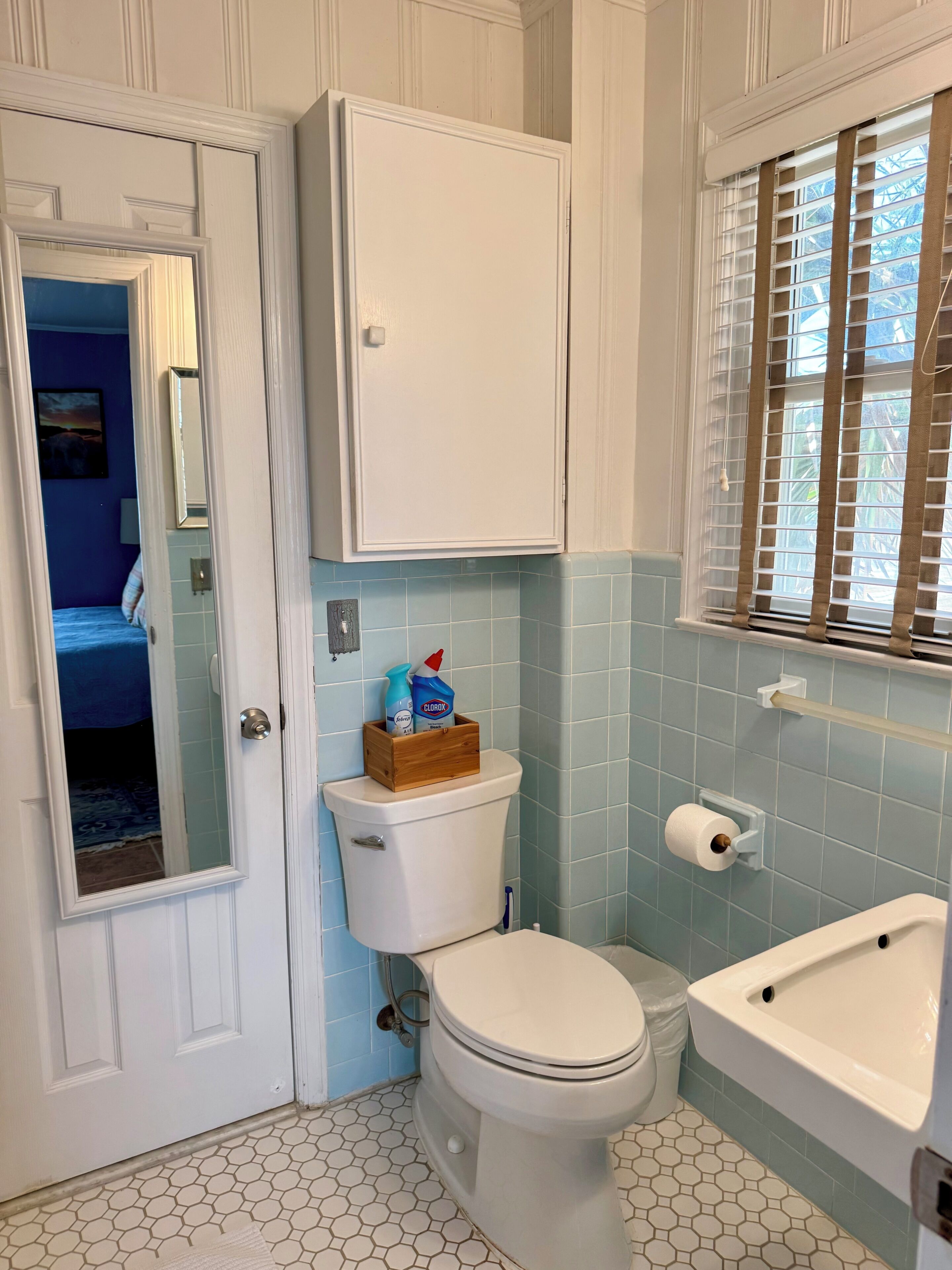 A bathroom with a toilet, sink, and window with blinds.