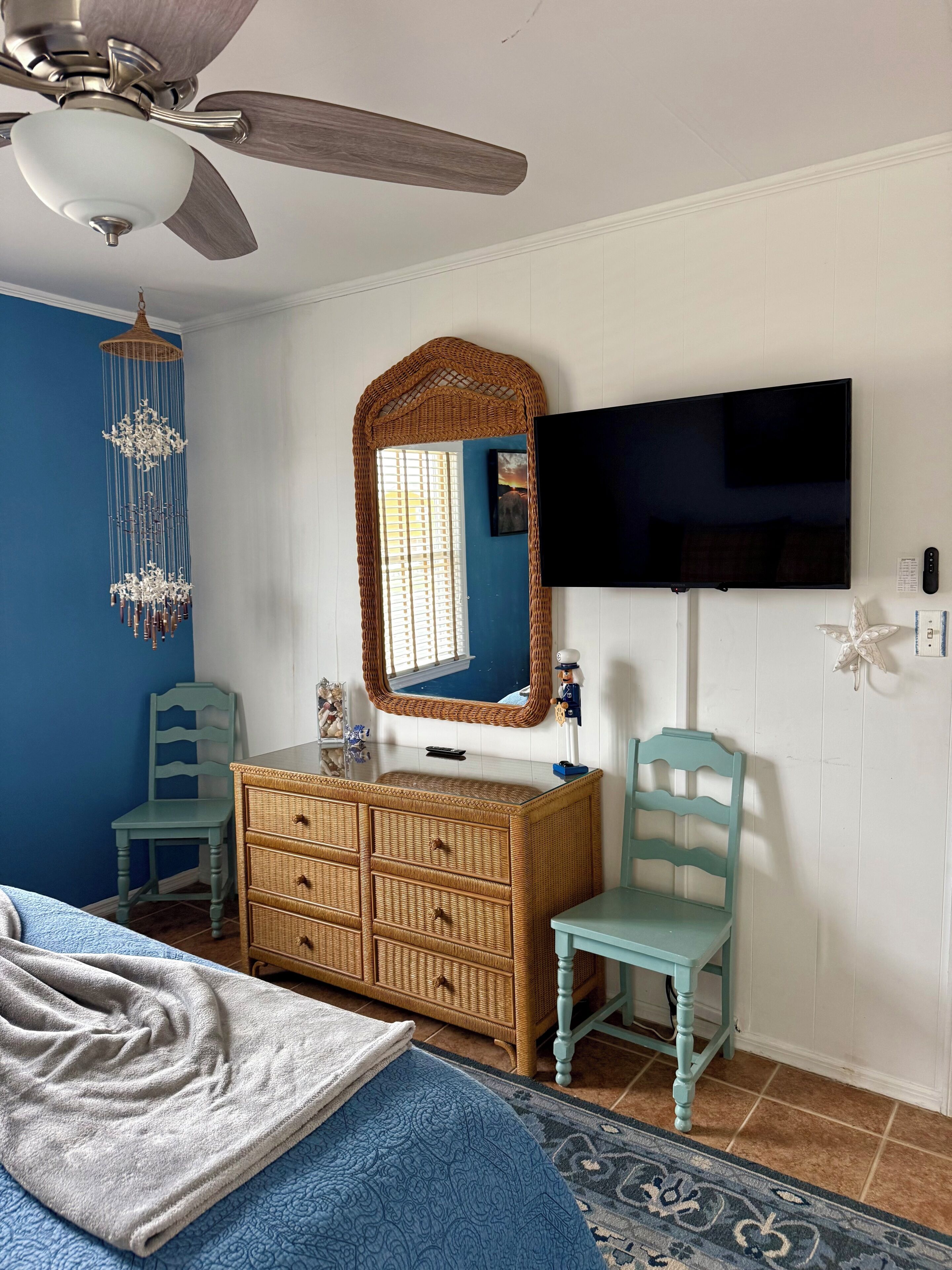 Un dormitorio con cama, cómoda, silla, televisor y ventilador de techo.