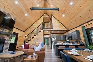 A modern interior with a wooden staircase leading to a loft bedroom, a cozy seating area, and a kitchen with dark cabinets. - Private pickleball / basketball court, hot tub at the Red River Gorge KY (Campton)