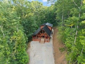 A cabin with a gravel driveway, surrounded by dense forest.