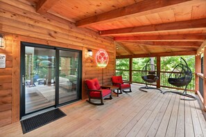 A wooden deck with rocking chairs and a hanging chair, a glass door entrance, and a neon sign. - Private pickleball / basketball court, hot tub at the Red River Gorge KY (Campton)