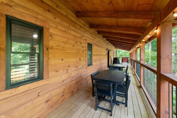A wooden cabin with a covered porch, a table with chairs, and a view of the surrounding forest.