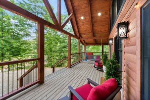 A wooden deck with a railing, a red chair, and a small Christmas tree. - Private pickleball / basketball court, hot tub at the Red River Gorge KY (Campton)