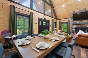 A dining area with a long wooden table set for four, a sofa, and a fireplace. - Private pickleball / basketball court, hot tub at the Red River Gorge KY (Campton)
