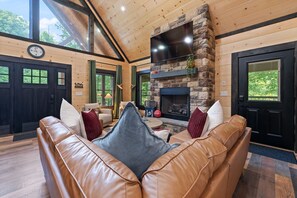 A cozy living room with a leather sofa, a fireplace, and a large window.