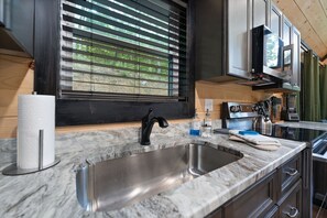 A kitchen with a stainless steel sink, a black faucet, and a window with blinds. - Private pickleball / basketball court, hot tub at the Red River Gorge KY (Campton)