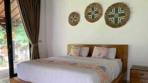A bedroom with a wooden bed, a nightstand, and decorative wall art. - Cozzy OMAH JEGEG Tabanan Bali (Marga)