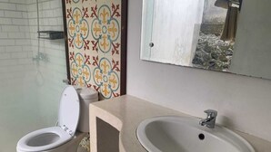 A bathroom with a toilet, sink, and a patterned wall. - Cozzy OMAH JEGEG Tabanan Bali (Marga)
