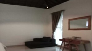 A room with a black sofa, a wooden desk, a mirror, and a window with curtains. - Cozzy OMAH JEGEG Tabanan Bali (Marga)