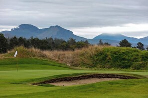 A golf course with a flag, bunkers, and a mountainous backdrop. - Gearhart House G637, second floor (Gearhart)