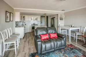 Une cuisine moderne avec des meubles blancs, un coin repas avec une table et des chaises, et un salon avec un canapé en cuir et un tapis coloré.