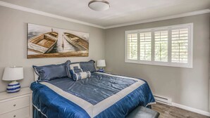 Een slaapkamer met een groot bed, twee wandlampen, een raam met luiken en een plafondventilator.