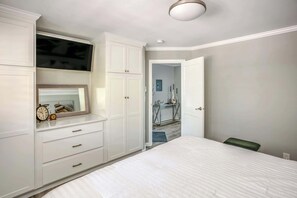 Une chambre à coucher comprenant un lit, une commode, un miroir et une porte donnant sur une autre pièce.
