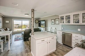 A modern kitchen with white cabinetry, a stainless steel dishwasher, and a large window offering a view of the outdoors. - Gearhart House G637, second floor (Gearhart)