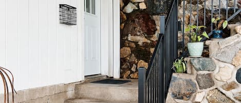 A stone staircase leading to a wooden deck with a white door and a metal railing.