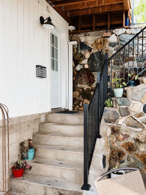 A stone staircase leading to a wooden deck with a white door and a metal railing.