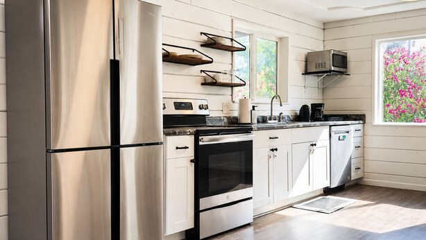 A modern kitchen with stainless steel appliances, white cabinetry, and a window with a view of pink flowers.