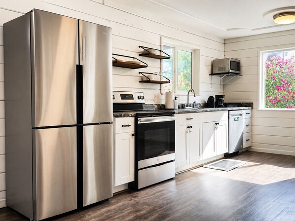 A modern kitchen with stainless steel appliances, white cabinetry, and a window with a view of pink flowers.