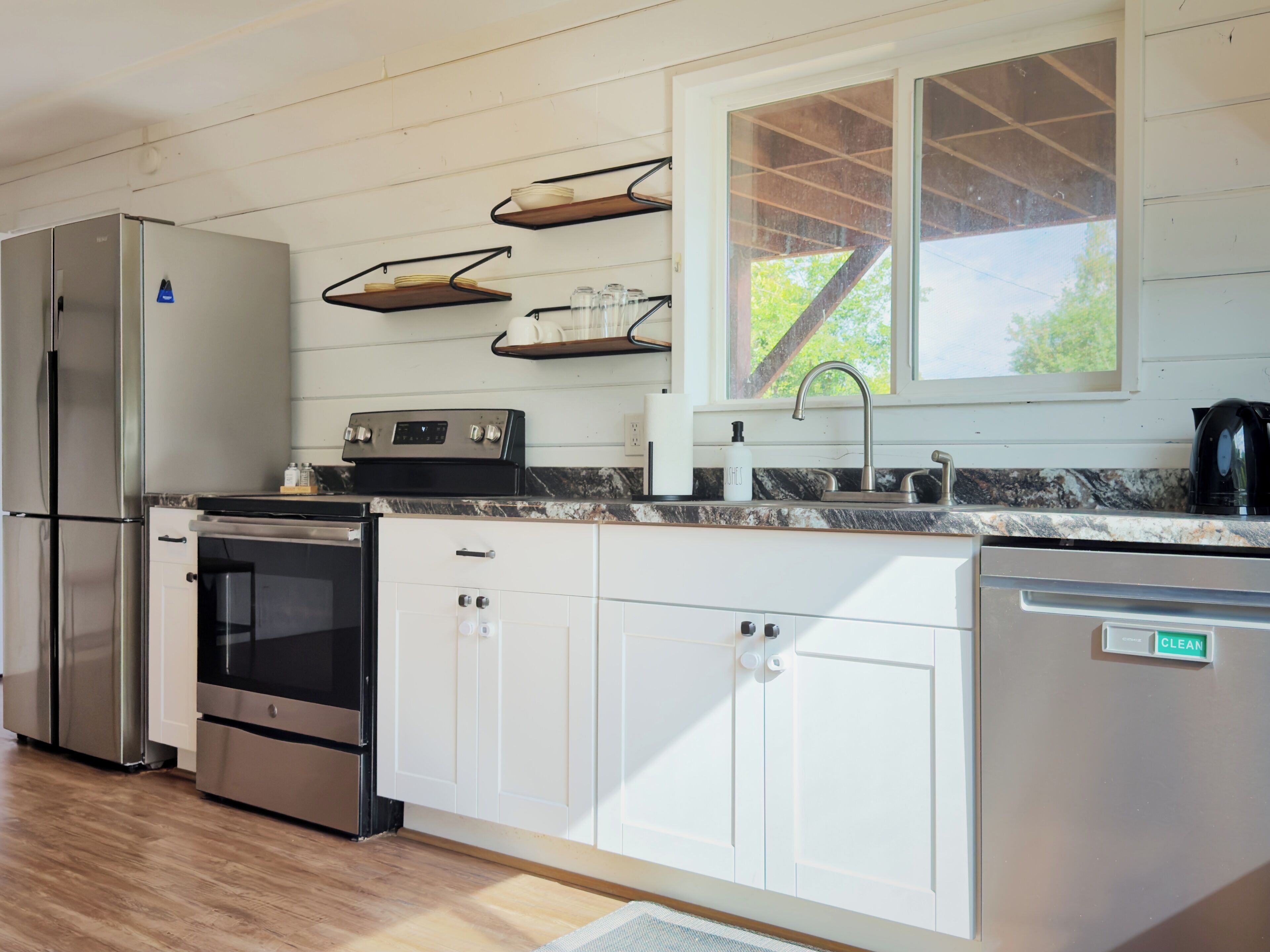 A modern kitchen with stainless steel appliances, white cabinetry, and a window with a view of greenery.