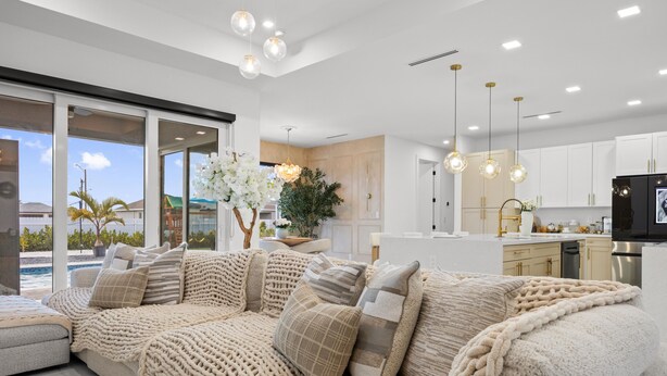 Ein modernes Wohnzimmer mit einem großen, beigefarbenen Sofa, einem Essbereich und einer Küche mit weißen Schränken.