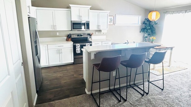 A kitchen with white cabinets, a central island with bar stools, a microwave, and a stove. - Charming 3-bedroom house with AC in Selah perfect for relaxing, small pets ok (Selah)