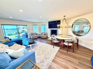 A modern living room with a blue sofa, a round dining table, and a fireplace. - Coastal Elegance - 2BDRM (Nanoose Bay)