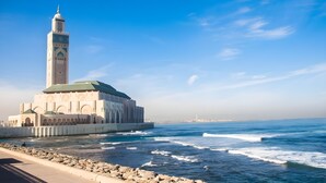 A coastal building with a prominent tower, a waterfront promenade, and a clear blue sky.