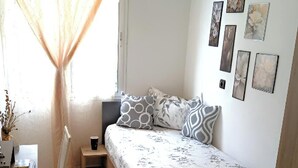 A bedroom with a bed, a chair, a desk, and a window with curtains.