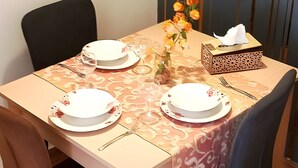 A dining table with floral tablecloth, chairs, and a vase with flowers.