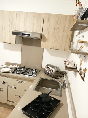 A kitchen with a gas stove, toaster, and a tray with black cups and a teapot.