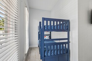 A room with a bunk bed, white blinds, and a view of the outside.