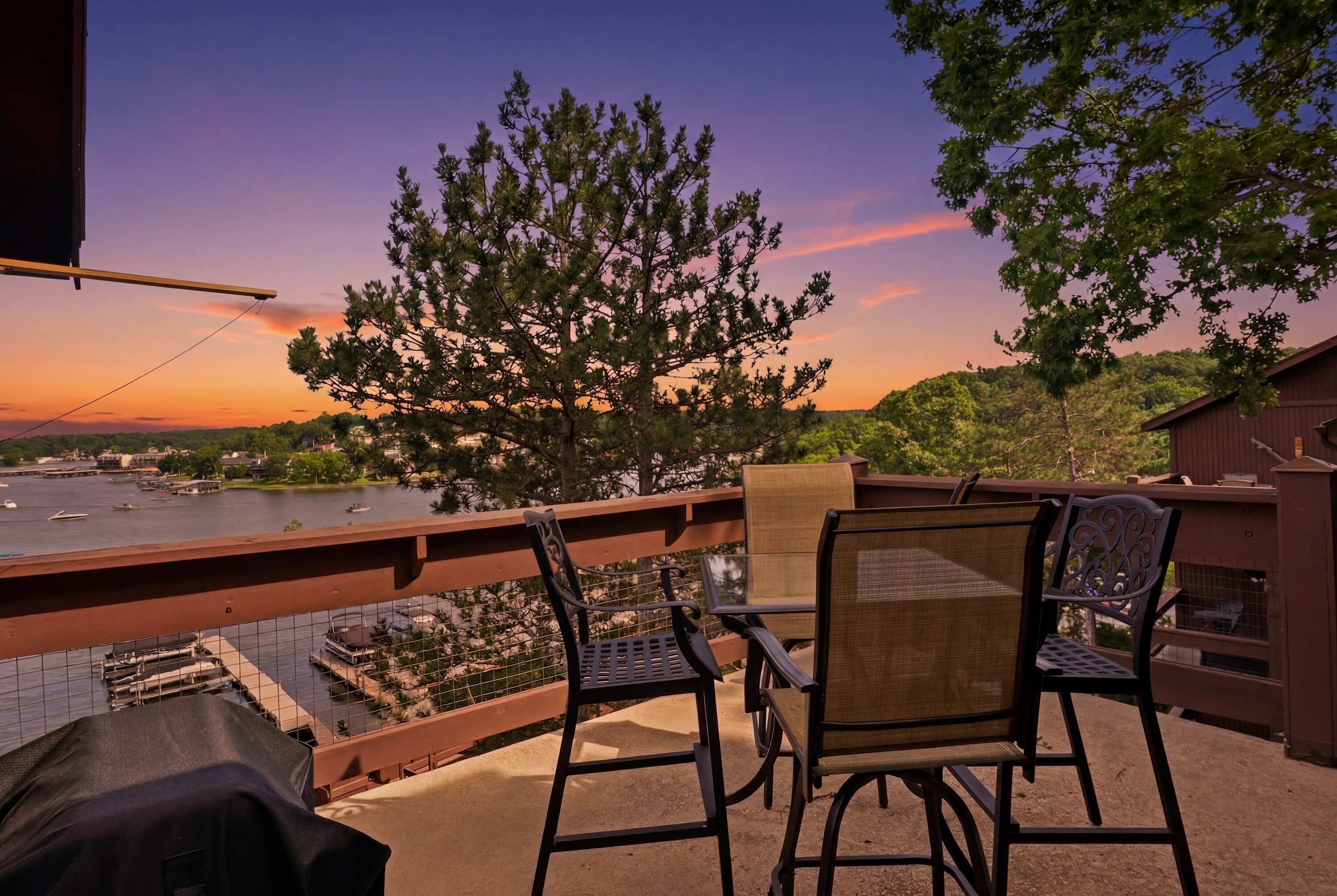 A balcony with two chairs, a view of a river, and a sunset.