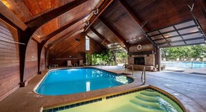 Une piscine intérieure dotée d’une cheminée en pierre, d’un plafond en bois et d’un espace extérieur abrité.