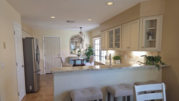 A kitchen with a central island, bar stools, a refrigerator, and a dining area with a chair. - Beautifully decorated single-level private townhome in the heart of Oro Valley. (Tucson)