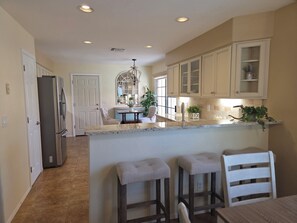 A kitchen with a central island, bar stools, a refrigerator, and a dining area with a chair. - Beautifully decorated single-level private townhome in the heart of Oro Valley. (Tucson)