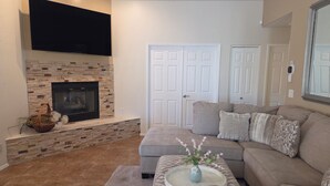 A living room with a fireplace, a flat-screen TV mounted above it, a sectional sofa, and a coffee table with a vase. - Beautifully decorated single-level private townhome in the heart of Oro Valley. (Tucson)