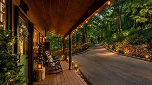 Eine Holzterrasse mit überdachtem Bereich, Sitzgelegenheiten im Freien und einem Pfad, der durch einen Wald führt.