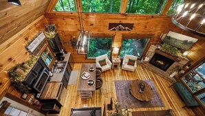 Ein Ferienhaus-Innenraum mit Küche, Essbereich, Sitzgelegenheiten, Kamin und großen Fenstern mit Blick auf einen Wald.