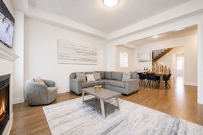 A spacious living room with a fireplace, a sectional sofa, a coffee table, and a dining area with a staircase.