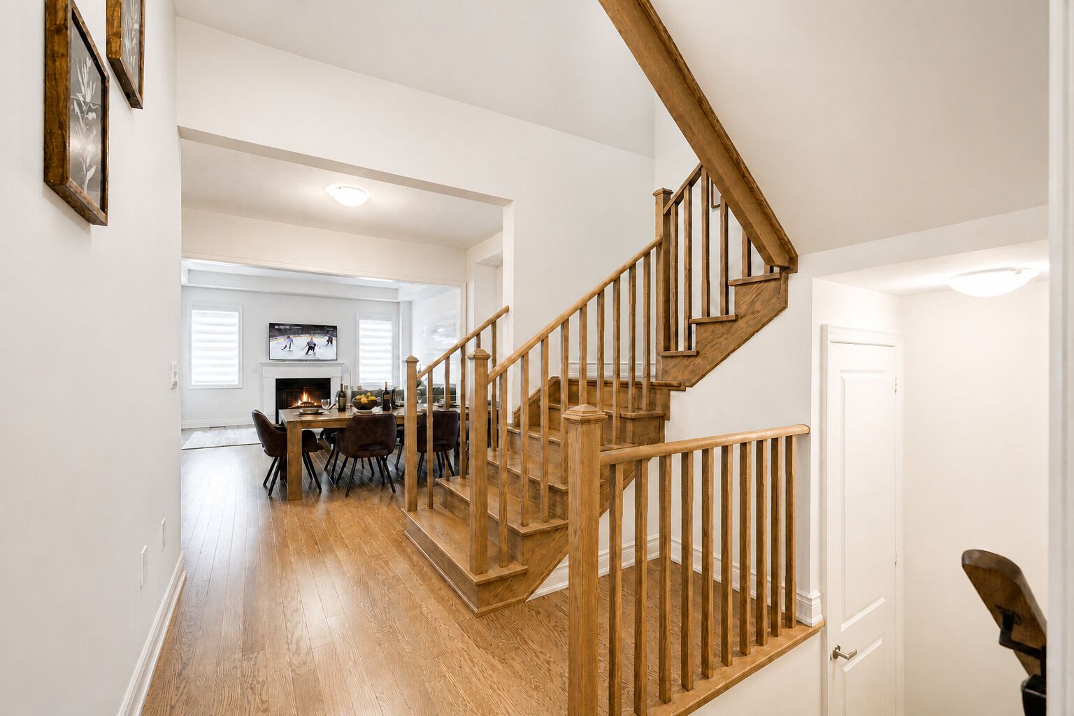Un escalier en bois menant à un deuxième étage, un coin repas avec une cheminée et un salon équipé d’un téléviseur.