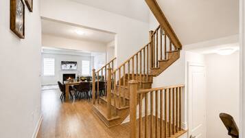 Un escalier en bois menant à un deuxième étage, un coin repas avec une cheminée et un salon équipé d’un téléviseur.