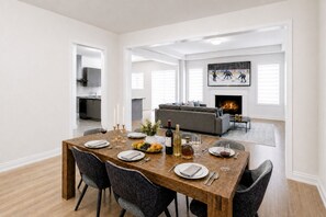 A dining area with a wooden table set for six, a grey sofa in the background, and a fireplace.