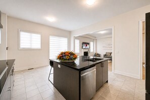 A modern kitchen with a central island, a dining area with a sofa, and a TV mounted on the wall.