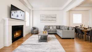 Una sala de estar con chimenea, un sofá modular, una mesa de centro y un comedor con una mesa lista para dos.