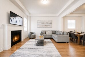 A living room with a fireplace, a sectional sofa, a coffee table, and a dining area with a table set for two.
