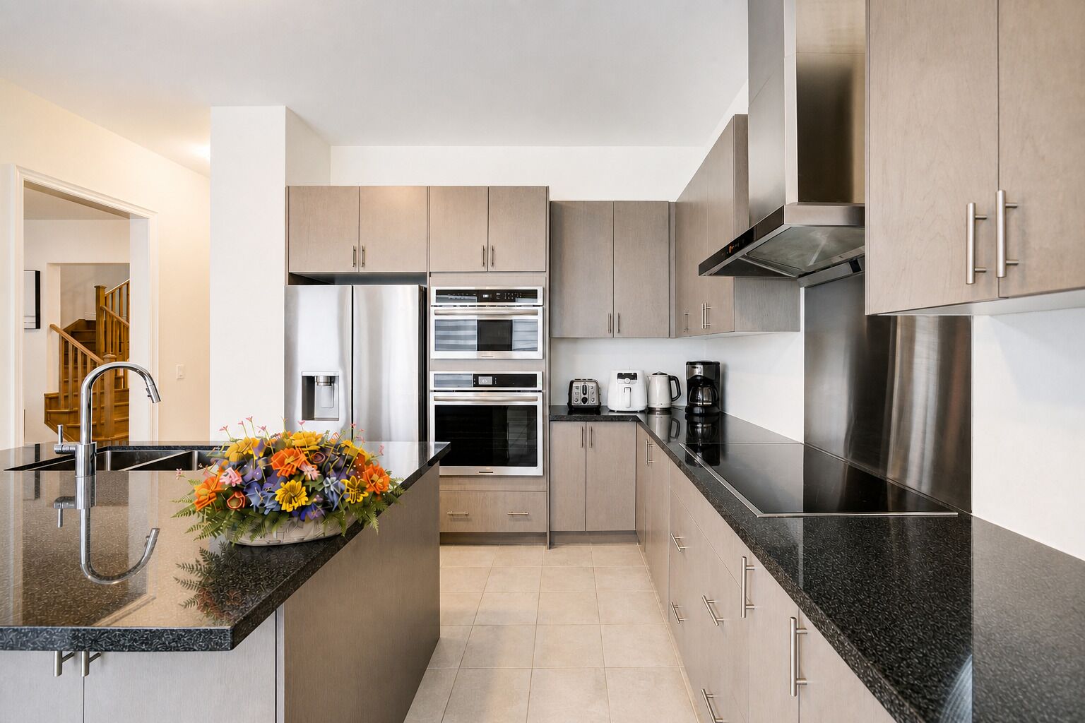 A modern kitchen with stainless steel appliances, a granite countertop, and light wood cabinets.